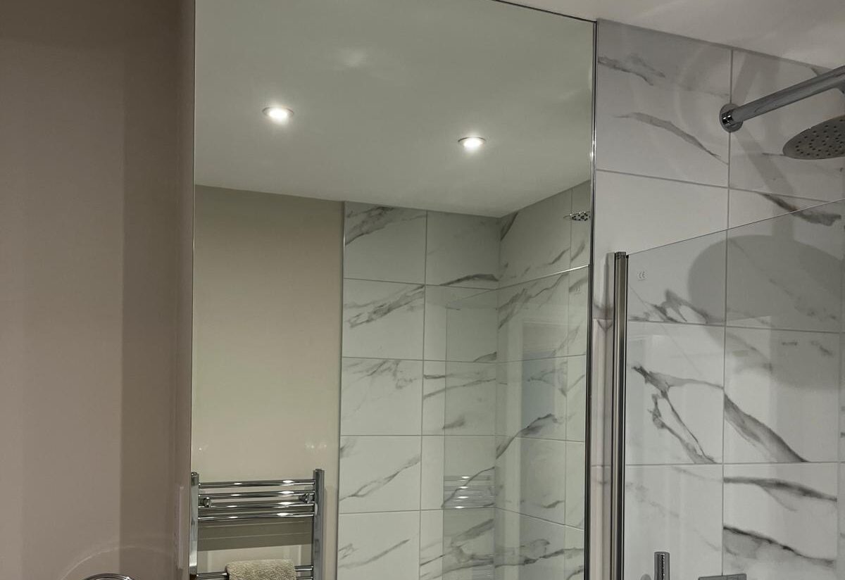 Wall-mounted silver mirror splashback installed above bathroom basin with tiled walls