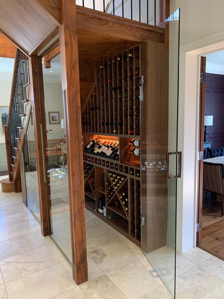 Bespoke frameless glass door fitted beneath staircase for a modern wine cellar entrance