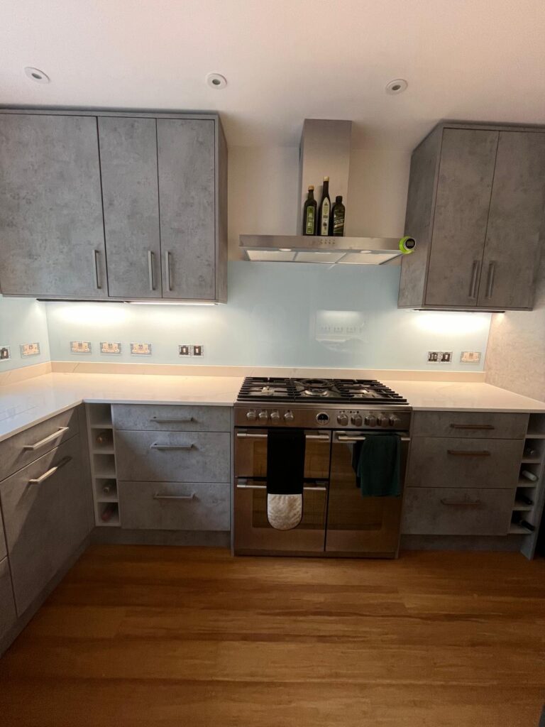 Light blue painted glass splashback installed behind gas hob in grey kitchen