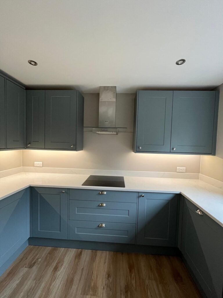 Painted taupe glass splashback fitted along hob run beneath blue shaker wall units