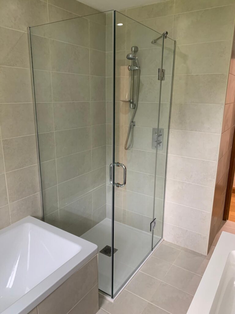 Minimalist frameless glass shower screen with chrome hinges and floor channel in a modern bathroom
