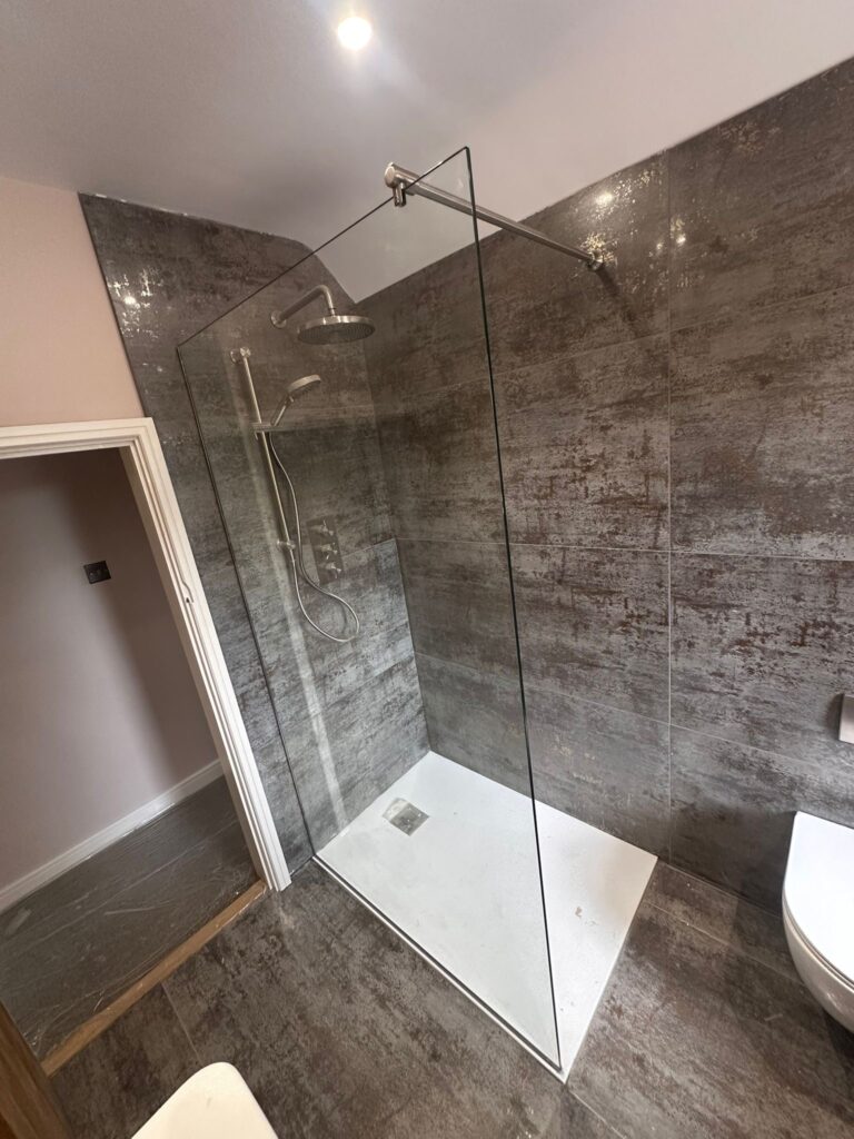 Frameless single glass shower screen installed in a modern tiled bathroom with chrome fittings
